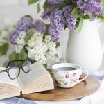 Vase of flowers with an open book, glasses, and teacup