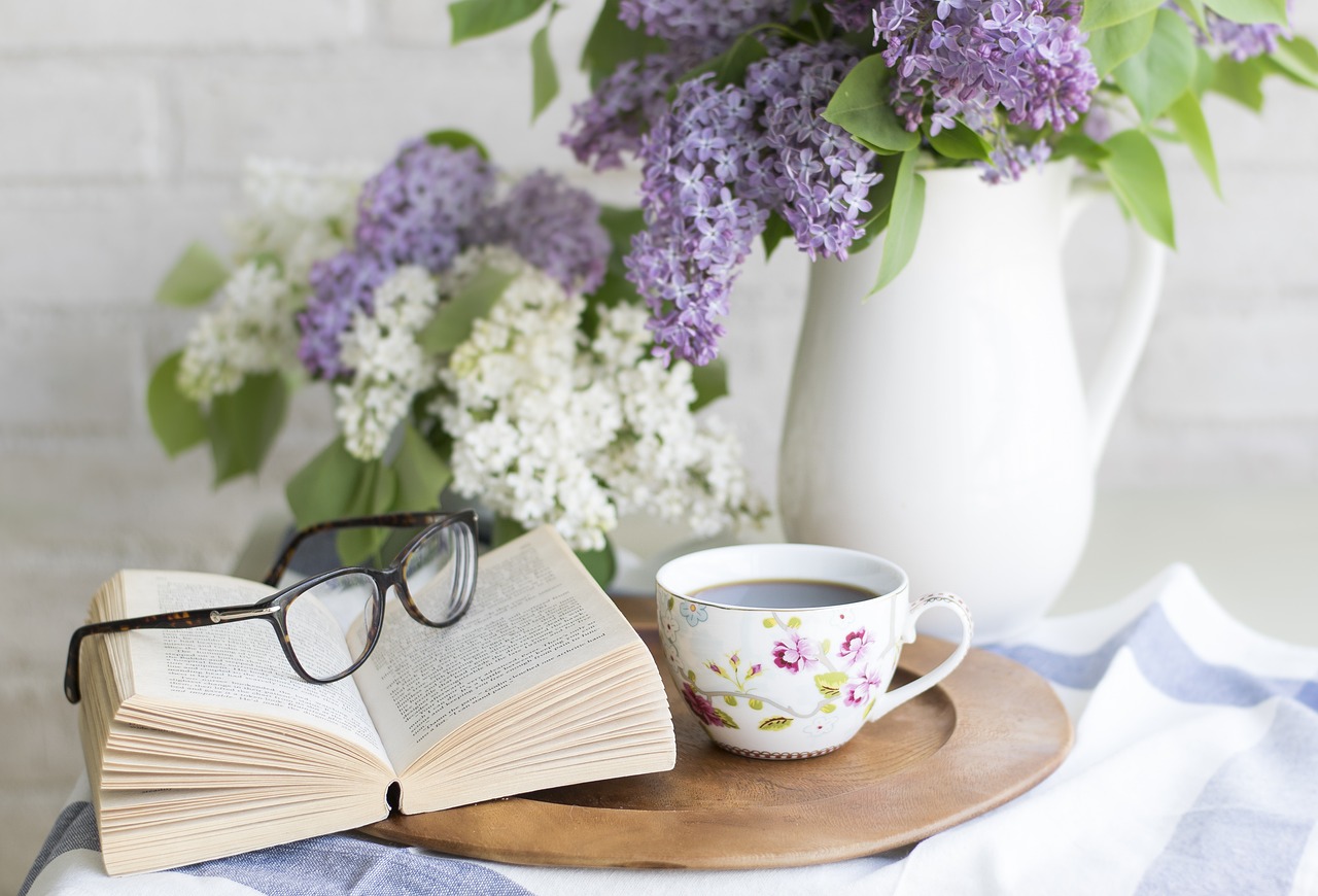 Vase of flowers with an open book, glasses, and teacup