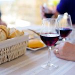 Photo of three people enjoying a picnic with red wine and a basket of bread