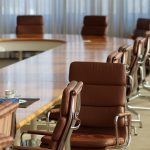 Photo of a conference room table with several empty brown leather chairs