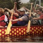 A picture of Susannah Plews paddling with teammates in the red boat.