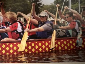 A picture of Susannah Plews paddling with teammates in the red boat.